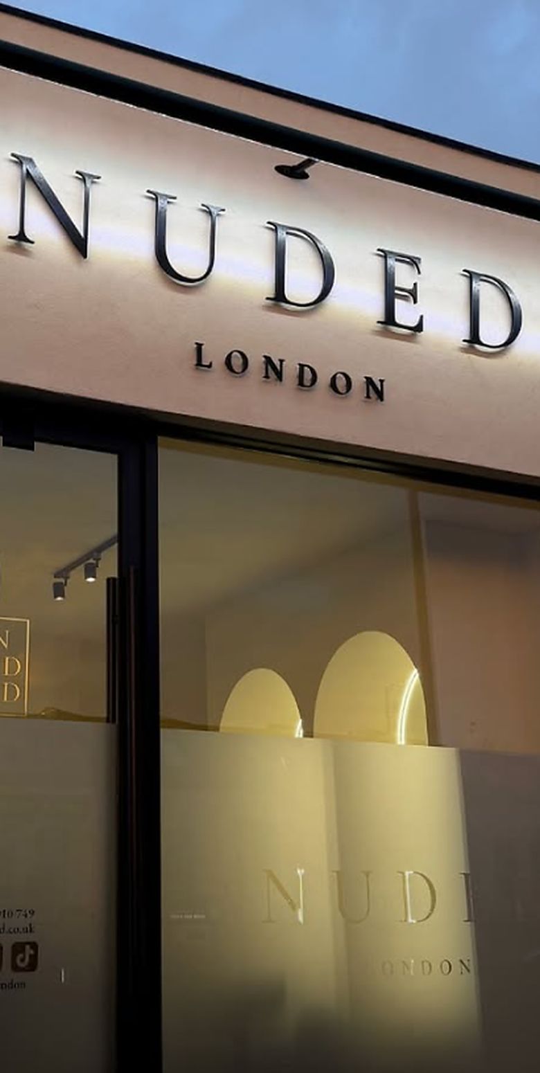 After: a pale fascia with backlit NUDED LONDON letters above full height glazing.